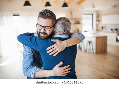 An adult son and senior father indoors at home, hugging.