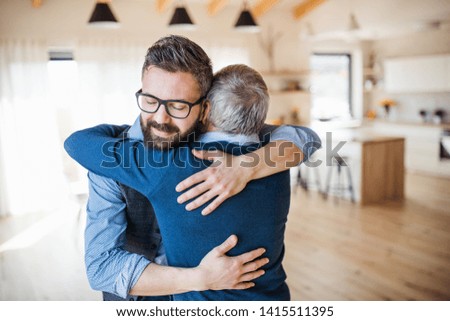 An adult son and senior father indoors at home, hugging.