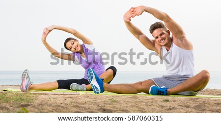 adult spanish  guy and girl practising yoga poses sitting on beach by sea at daytime