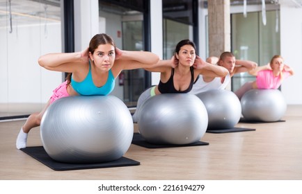 Adult Sports People Practiciting Pilates In The Studio During A Group Training Session Perform An Exercise On A Fitness Ball, ..which Strengthens The Lumbar Region And Develops Overall Flexibility