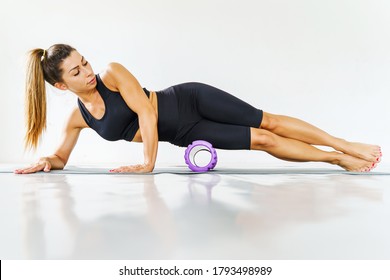 Adult sporty woman doing fascia exercise on the floor - Caucasian female using foam massage roller - tool for leg thigh tension and muscle pain release - physical therapy and training concept