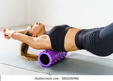 Adult sporty woman doing fascia exercise on the floor - Caucasian female using foam massage roller - tool for back tension and muscle pain release - physical therapy and training stretch concept