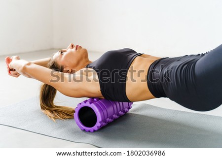 Adult sporty woman doing fascia exercise on the floor - Caucasian female using foam massage roller - tool for back tension and muscle pain release - physical therapy and training stretch concept