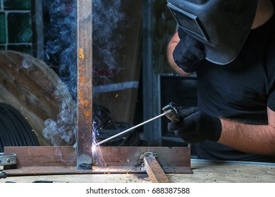 Adult Strong man in a black welding mask welds a arc welding machine metal in a dark old garage, working with a welding machine, around a lot of tools for work