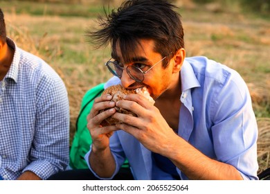 The Adult Student Is Eating A Burger Outdoors