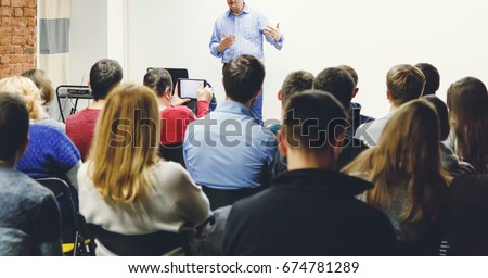 Adult students listen to professor's lecture in small class room. Rear view, panoramic aspect ratio.