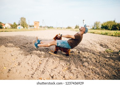 Adult Stylish Man Riding  Toy Horse On Field Outdoor. Young Funny Unusual Strange Male Person With Smiling Face Lifestyle Portrait. Odd Happy Boy Childhood Memories. Adult Acting Like A Child Concept.