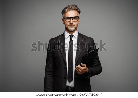 Adult successful employee business man corporate lawyer wears classic formal black suit shirt tie work in office hold clipboard with paper account documents isolated on plain grey background studio