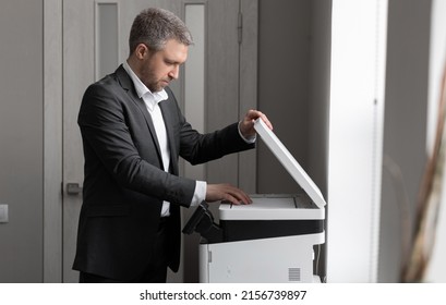 An Adult Successful Man In A Gray Business Suit Stands Near A Copier