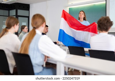 Adult teacher in the classroom shows the students the flag of the Netherlands at a geography lesson