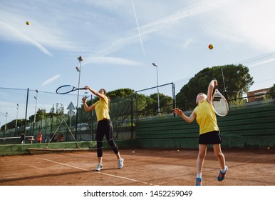 An Adult tennis player and a child tennis player serving a ball at the tennis court on the sunset, wearing yellow t-shirts  - Powered by Shutterstock