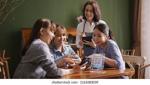 Adult waiter staff casual apron SME owner enjoy work listen to young asia people smile fun talk look at smart QR code on mobile app eat vegan meal after reopen coffee shop food drink inside cafe bar.