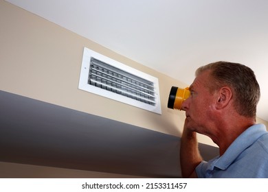 Adult white man with a flashlight inspecting a rectangle wall air vent duct near a ceiling. Caucasian male looking into an outflow HVAC air vent duct with a flashlight to inspect for any maintenance.