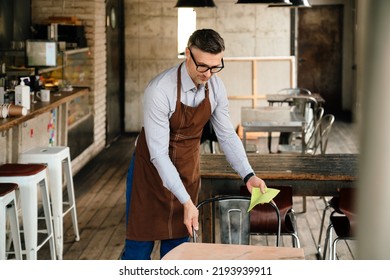 Adult White Waiter Wearing Apron And Eyeglasses Cleaning Tables While Working In Cafe Indoors