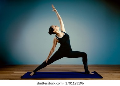 Adult Woman 45-55 Years Old In Good Shape Doing Yoga Posing On A Blue Studio Background With A Wooden Floor On A Training Mat. Yoga, Stretching, Healthy Lifestyle.