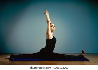 Adult Woman 45-55 Years Old In Good Shape Doing Yoga Posing On A Blue Studio Background With A Wooden Floor On A Training Mat. Yoga, Stretching, Healthy Lifestyle.