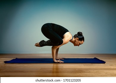 Adult Woman 45-55 Years Old In Good Shape Doing Yoga Posing On A Blue Studio Background With A Wooden Floor On A Training Mat. Yoga, Stretching, Healthy Lifestyle.