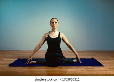 Adult Woman 45-55 Years Old In Good Shape Doing Yoga Posing On A Blue Studio Background With A Wooden Floor On A Training Mat. Yoga, Stretching, Healthy Lifestyle.