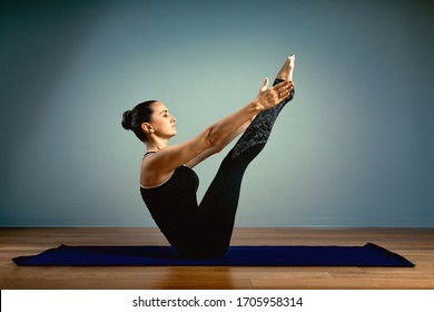 Adult Woman 45-55 Years Old In Good Shape Doing Yoga Posing On A Blue Studio Background With A Wooden Floor On A Training Mat. Yoga, Stretching, Healthy Lifestyle.