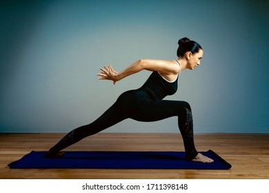 Adult Woman 45-55 Years Old In Good Shape Doing Yoga Posing On A Blue Studio Background With A Wooden Floor On A Training Mat. Yoga, Stretching, Healthy Lifestyle.