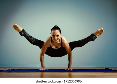 Adult Woman 45-55 Years Old In Good Shape Doing Yoga Posing On A Blue Studio Background With A Wooden Floor On A Training Mat. Yoga, Stretching, Healthy Lifestyle.