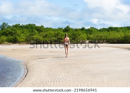 An adult woman in a bikini walking under strong sunlight on Guaibim beach in the city of Valenca, Brazilian state of Bahia. Travel and fun.