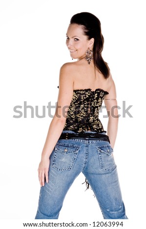 Adult woman in a black and gold corset and tight fitting blue jeans with her back to the camera smiling over her shoulder