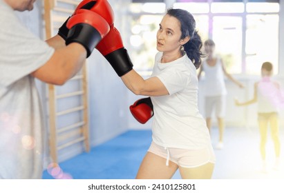 Adult woman in boxing gloves sparring with husband in gym, while preteen children, daughter and son, enthusiastically jumping rope in background. Active lifestyle and shared family sports activities - Powered by Shutterstock