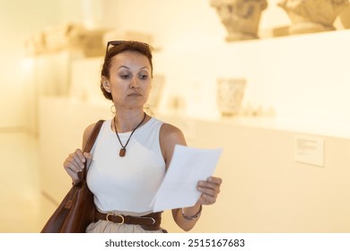 Adult woman with brochure looking at antique exhibit in museum hall.. - Powered by Shutterstock