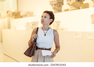 Adult woman with brochure looking at antique exhibit in museum hall.. - Powered by Shutterstock