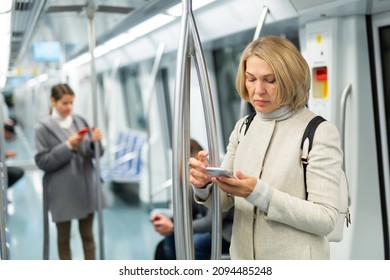 Adult woman browsing and typing messages on tablet in subway car leaning on handrail. High quality photo