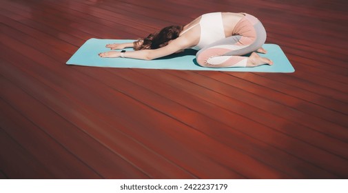 Adult woman in a child's pose on a yoga mat, wearing a white and pink yoga outfit on a red wooden deck, peaceful and relaxed, with a focus on wellness and mindfulness - Powered by Shutterstock