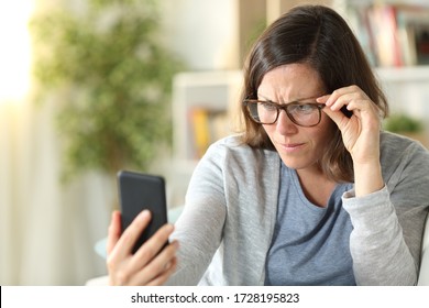 Adult Woman With Eyesight Problems Wearing Eyeglasses Reading On Smart Phone Sitting On A Couch At Home