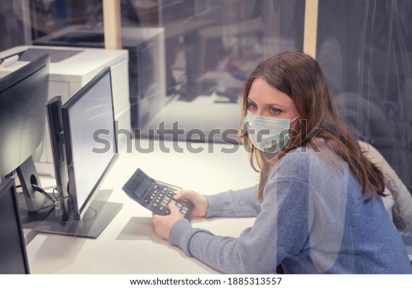 Adult woman in a face mask works in an office\
behind a glass partition. Work in the office with protection from\
the virus during the flu\
epidemic