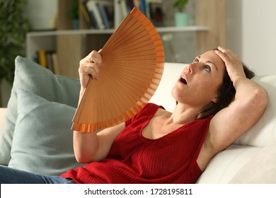 Adult woman fanning suffering heat stroke sitting in the livingroom at home - Shutterstock ID 1728195811