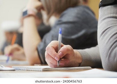 An adult woman with a fountain pen sits next to colleagues and writes in a notebook during a meeting or professional development training session.Photo. No face. Selective focus. Close-up - Powered by Shutterstock