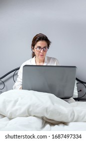 Adult Woman With Glasses, Working At Home Working At Home In Her Pijama With A Laptop And A Mobile Phone. Work From Home Concept