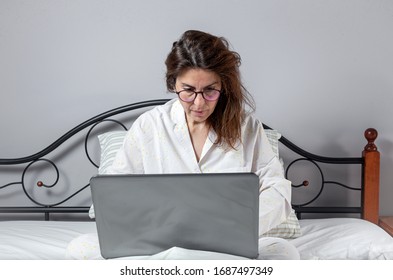 Adult Woman With Glasses, Working At Home Working At Home In Her Pijama With A Laptop And A Mobile Phone. Work From Home Concept