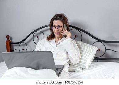 Adult Woman With Glasses, Working At Home Working At Home In Her Pijama With A Laptop And A Mobile Phone. Work From Home Concept