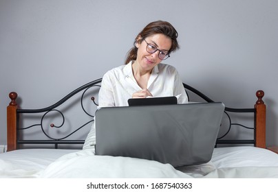 Adult Woman With Glasses, Working At Home Working At Home In Her Pijama With A Laptop And A Mobile Phone. Work From Home Concept