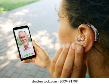 Adult woman with a hearing aid in her ear communicates with her father via video communication via a smartphone. Full human life with hearing aids