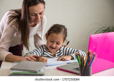 Adult woman helping ethnic girl to do homework assignment in notebook near laptop during studies at home