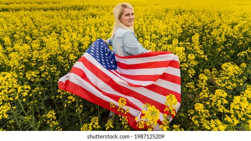 Adult Woman Holding American Flag With Pole, Stars And Stripe In A Yellow Rapeseed Field. USA Flag Fluttering In The Wind