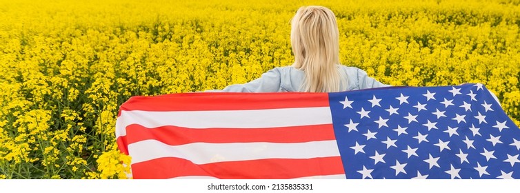 Adult Woman Holding American Flag With Pole, Stars And Stripe In A Yellow Rapeseed Field. USA Flag Fluttering In The Wind