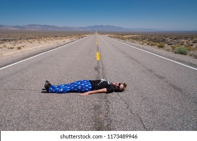 Adult Woman Lays Down In The Middle Of The Road (Extraterrestrial Highway In Nevada's Desert). Concept For Daring, Daredevil, Dare, Open Road