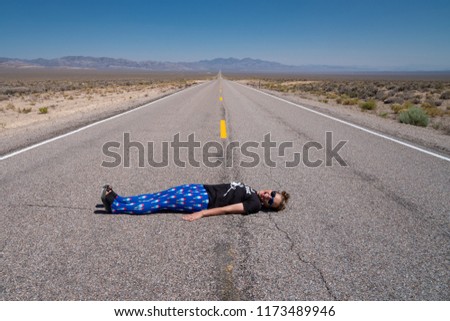 Adult woman lays down in the middle of the road (Extraterrestrial Highway in Nevada's desert). Concept for daring, daredevil, dare, open road