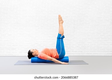 Adult Woman Lying On Back Along Foam Roller With Straight Legs Up And Practice Pilates In Fitness Studio, Indoor