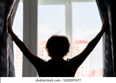erwachsene Frau öffnet die Vorhänge des Fensters und blickt auf den nächsten Tag