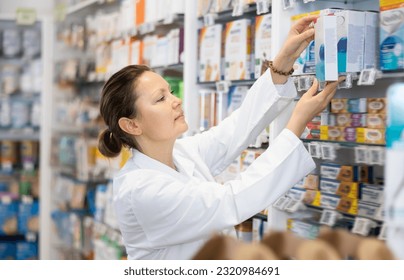 Adult woman pharmacist in uniform arranges products on shelves in pharmacy.. - Powered by Shutterstock