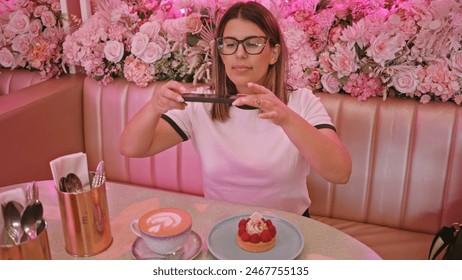 Adult woman photographing desserts in a pink floral-designed cafe - Powered by Shutterstock